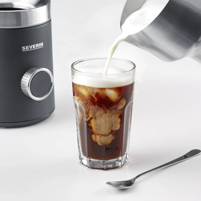 Kall bryggkaffe med mjölk hälls i glas, Severin mjölkskummare, sked bredvid på vit bakgrund